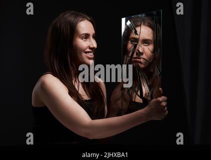 Non mi conoscete, una donna creepy che grinning alla sua riflessione in uno specchio rotto. Foto Stock