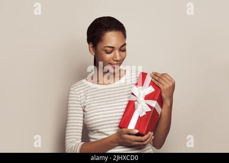 Felice giovane donna afroamericana con regalo rosso scatola nelle sue mani su sfondo bianco Foto Stock