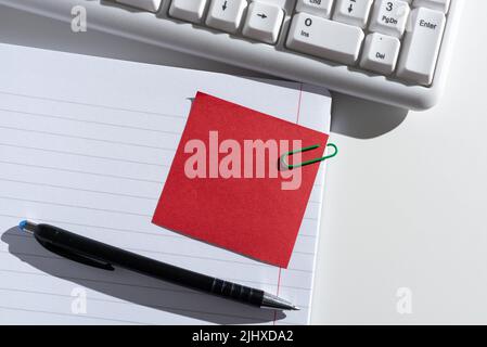 Nota adesiva con messaggio importante tagliato sul notebook aperto sulla scrivania con penna e tastiera. Informazioni Crutial presentate su Memo allegato su blocco note Foto Stock