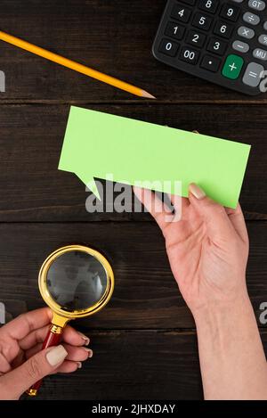 Mani di Businesswoman con carta di bolla di pensiero e cancelleria su sfondo di legno. Donna che tiene il foglio di colore pastello con spazio di copia per il commercio Foto Stock