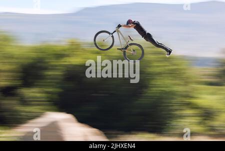 Giovane uomo che mostra le sue abilità ciclistiche mentre fuori in bicicletta su una bicicletta fuori. Adrenalina junkie praticare un salto di sporcizia all'aperto. Maschio che indossa un casco Foto Stock