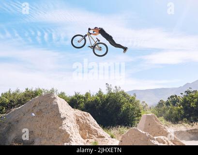 Giovane uomo che mostra le sue abilità ciclistiche mentre fuori in bicicletta su una bicicletta fuori. Adrenalina junkie praticare un salto di sporcizia all'aperto. Maschio che indossa un casco Foto Stock