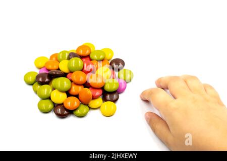 Mano del bambino che raggiunge per le caramelle o il bonbon. Caramelle colorate e la mano dei bambini su sfondo bianco Foto Stock