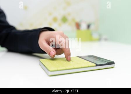 Donna d'affari che punta sulla calcolatrice sulla scrivania con notebook. Donna che preme sul fondo del tavolo con blocco note. Executive Visualizza informazioni recenti. Foto Stock