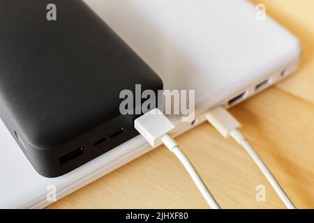Power Bank carica un computer portatile tramite cavo USB di tipo C su sfondo in legno Foto Stock