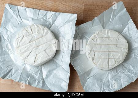 Due teste di formaggio Camembert su carta bianca su tagliere. Preparazione per la cottura alla griglia Foto Stock