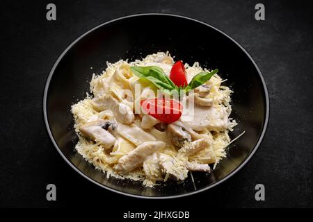 Fetuchini alfredo con funghi e pollo in salsa cremosa al formaggio. Su sfondo nero Foto Stock