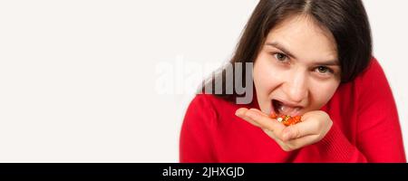 Una donna in rosso mangia un sacco di pillole guardando nella macchina fotografica, medicina in una manciata di palme. Banner con posizione per il testo. Foto Stock