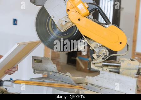 C'è un operaio che taglia modanature di legno su sega circolare per completare il lavoro di finitura su una casa Foto Stock