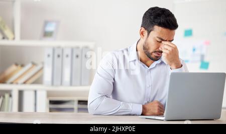 Giovane uomo d'affari misto di razza che soffre di un mal di testa che lavora su un notebook in un ufficio solo al lavoro. Un uomo ispanico che si stressava mentre lavorava. Maschio Foto Stock