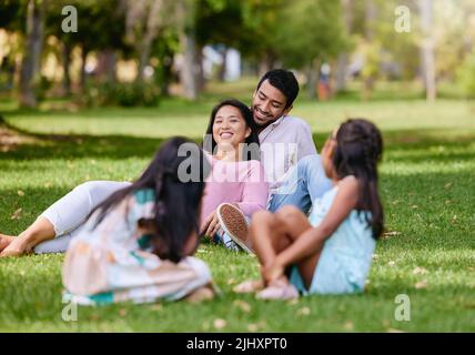 Ritratto di felice coppia asiatica giacente insieme sull'erba. I bambini giocano mentre guardano i loro genitori che amano passare del tempo insieme al parco Foto Stock