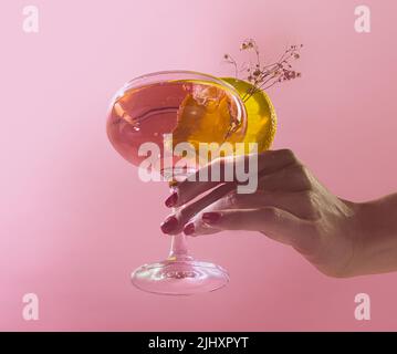 Bicchiere femminile di delizioso cocktail alcolico con acqua di rose e spumante isolato su sfondo rosa Foto Stock
