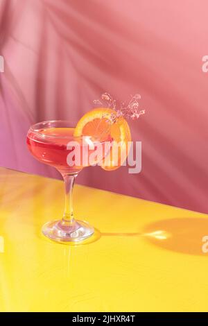 Bicchiere di delizioso cocktail alcolico con acqua di rose e spumante isolato su sfondo giallo rosa Foto Stock