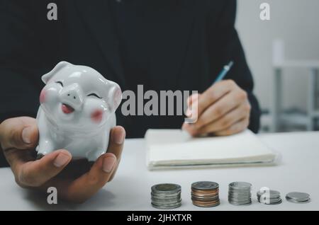 Uomo d'affari persona tenuta a mano risparmio piggybank moneta denaro su table.Business conto finanziario investimento fiscale economia assicurazione e piano di pensionamento con Foto Stock