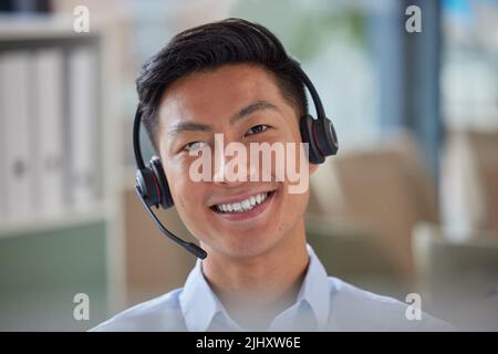Primo piano ritratto di un amichevole uomo d'affari asiatico che lavora in un call center. Consulente finanziario che indossa una cuffia con microfono. Addetto all'assistenza clienti Foto Stock