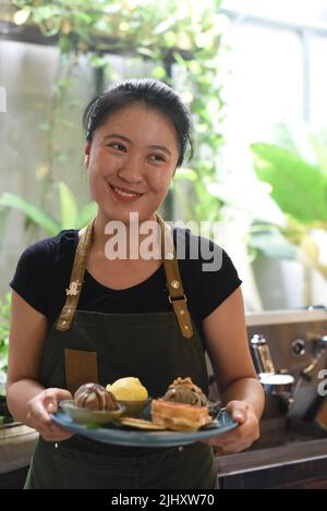 Ragazza vietnamita che serve gelato fatto in casa con waffle in una caffetteria Foto Stock