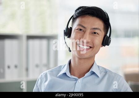 Uomo d'affari asiatico che lavora in un call center e sorride in un ufficio luminoso. Consulente finanziario che indossa un auricolare. Il rappresentante del servizio clienti è molto positivo Foto Stock