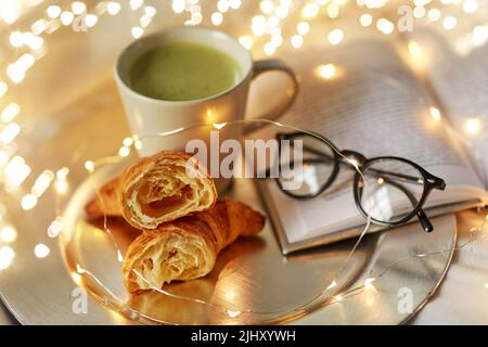 croissant, tè matcha, libro e bicchieri a letto Foto Stock