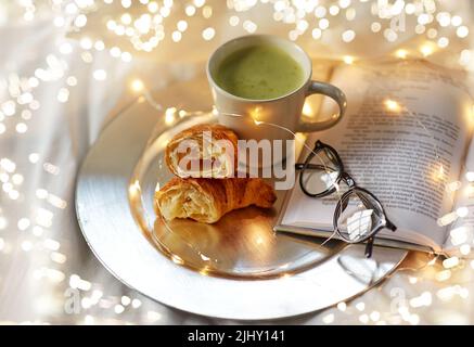 croissant, tè matcha, libro e bicchieri a letto Foto Stock
