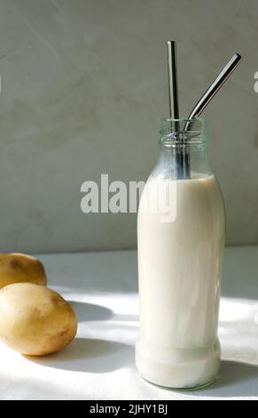 Bottiglia di vetro con tubi metallici e latte di patate sul tavolo. Una nuova tendenza nel mangiare sano. Concetto di cibo alternativo. Latte vegetale per vegani. Verti Foto Stock