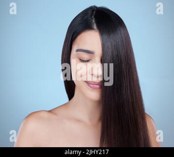 Ama le serrature in cui ti sei. Studio girato di una bella giovane donna mostrando i suoi lunghi capelli setosi su uno sfondo blu. Foto Stock
