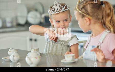 Due bambine che hanno una festa del tè della principessa a casa. Amici fratelli sorelle che indossano le tiaras mentre giocano con il set di tè e hanno biscotti in cucina Foto Stock