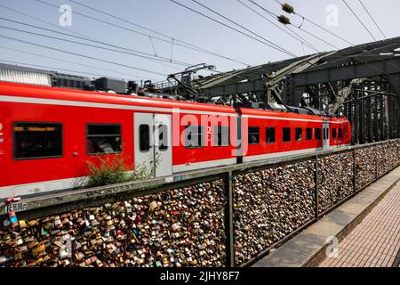 Lucchetti sulla recinzione del ponte ferroviario Hohenzollern con treno di passaggio, Colonia, Germania Foto Stock