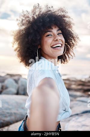 Una giovane donna mista che sorride sulla spiaggia mentre si allunga la mano. Felice ispanica femmina con un fresco afro acconciatura all'aperto Foto Stock