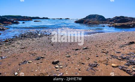 Onde sulla spiaggia sabbiosa con pezzi di vetro lucenti Foto Stock