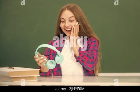 sorprendo ragazza teen tenere cuffie moderne in high school a lavagna, scuola Foto Stock