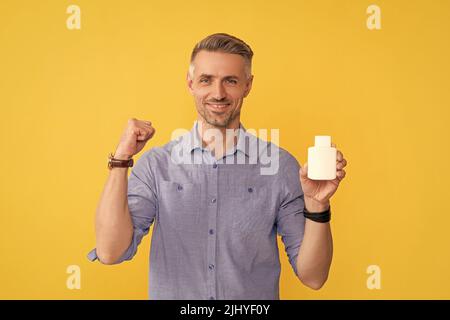 ragazzo felice che mostra la bottiglia di vitamina su sfondo giallo, supplemento Foto Stock