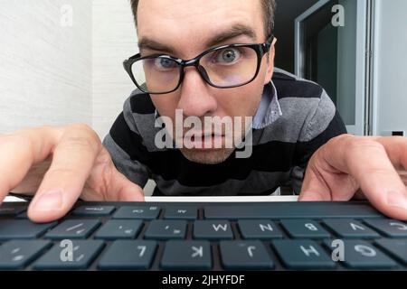 Uomo pazzo che digita sulla tastiera e guarda la fotocamera. Uomo sorpreso al lavoro Foto Stock