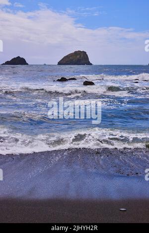 Onde che colpiscono la spiaggia di sabbia nera sulla costa occidentale Foto Stock