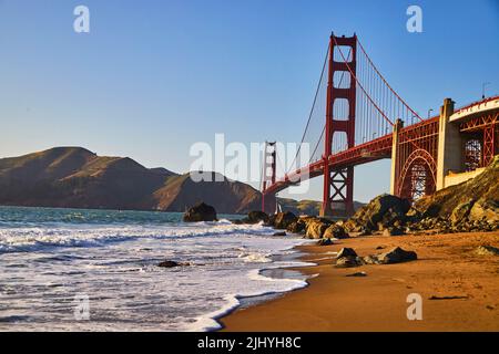 Ondeggia sulle spiagge sabbiose al Golden Gate Bridge vicino al tramonto Foto Stock