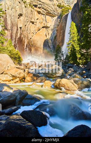 Yosemite sbalorditive cascate inferiori in primavera con l'arcobaleno e cascata fiume ghiacciato Foto Stock