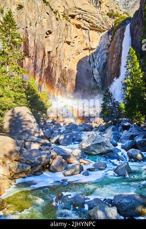 Cascate di Yosemite con acque gelide su rocce e arcobaleno Foto Stock