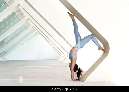 Donna che fa un cavalletto contro un arco di cemento. Esercitarsi all'aperto. Foto Stock