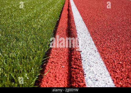 Sfondo dello stadio sportivo. Pista di corsa in gomma artificiale rossa e linea bianca e campo sportivo di calcio in erba sintetica verde Foto Stock