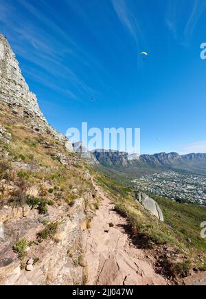 Parapendio da Lions Head con una splendida vista di Table Mountain a Città del Capo, Sud Africa. Lussureggianti alberi verdi che crescono in armonia su terreni rocciosi Foto Stock