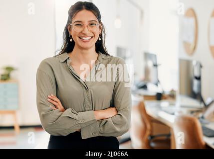 M più sicuro nel mio posto di lavoro. Una giovane donna d'affari attraente in piedi da sola nell'ufficio con le sue braccia piegate. Foto Stock