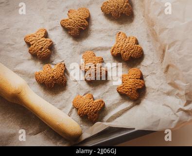 Su un foglio da forno su carta da forno sono farina d'avena biscotti fatti in casa sotto forma di uomini di pan di zenzero, e accanto ad esso è un perno di rotolamento. Cucina casalinga. Dolce pa Foto Stock