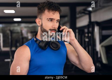 Bel maschio con tatuaggi nel suo 20s parlando al telefono in palestra Foto Stock