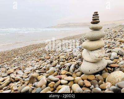 Una piramide di ciottoli sulla riva sotto un cielo blu Foto Stock