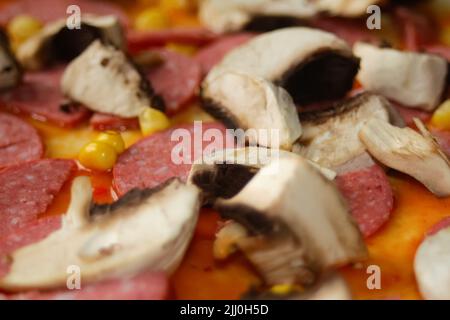 Defocalizzare gli ingredienti del primo piano per la pizza sull'impasto. Salsa di pomodoro rosso, salsicce, mais dolce. Pizza italiana fatta in casa. Home culinario. Sfocato. Cucina italiana Foto Stock