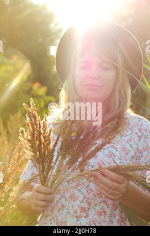 Sfocare primo piano ritratto esterno di bella giovane bionda donna su sfondo natura. Donna che tiene mazzo di pampas erba. Salute mentale, all'aperto. Li Foto Stock