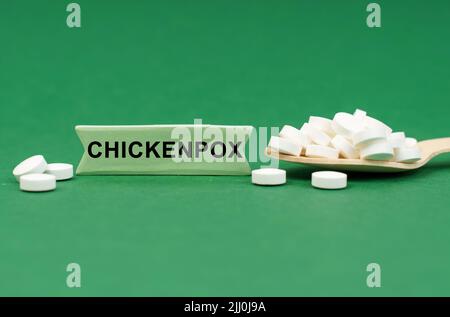 Concetto di medicina. Su una superficie verde, un cucchiaio di legno con pillole e un segno con l'iscrizione - LA VARICELLA Foto Stock