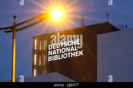 21 luglio 2022, Sassonia, Lipsia: La nuova scritta "Deutsche Nationalbibliothek" (DNB) brilla su un edificio alto 55 metri dell'ex biblioteca tedesca con un lampione in primo piano. Il logo da 7,7 x 3,2 metri è costituito da un corpo in alluminio verniciato e vetro acrilico illuminato da dietro. È montato sulla terza estensione dell'edificio DNB a Lipsia, il Bücherturm, inaugurato nel 1982. Una scritta identica deve ancora essere installata sul lato est del caricatore. La Biblioteca Nazionale tedesca, con sedi a Lipsia e Francoforte sul meno, raccoglie tutto ciò che è pubblicato nella Foto Stock