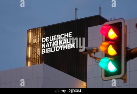 21 luglio 2022, Sassonia, Lipsia: La nuova scritta "Deutsche Nationalbibliothek" (DNB) brilla su un edificio alto 55 metri dell'ex biblioteca tedesca con un semaforo in primo piano. Il logo da 7,7 x 3,2 metri è costituito da un corpo in alluminio verniciato e vetro acrilico illuminato da dietro. È montato sulla terza estensione dell'edificio DNB a Lipsia, il Bücherturm, inaugurato nel 1982. Una scritta identica deve ancora essere installata sul lato est del caricatore. La Biblioteca Nazionale tedesca, con sedi a Lipsia e Francoforte sul meno, raccoglie tutto ciò che è pubblicato in G. Foto Stock