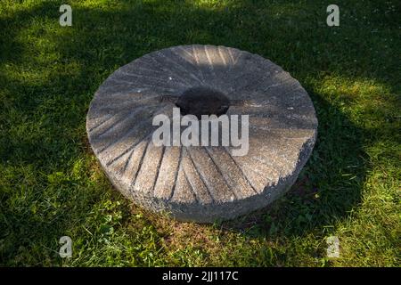 Macina per grano macinando o grani altri. Macinando pietre. Vecchio elemento di mulino su erba verde Foto Stock