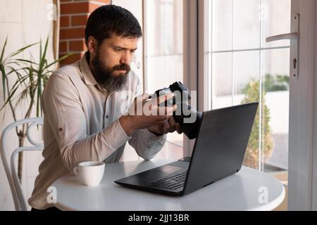 Fotografo creativo che lavora con laptop e fotocamera digitale al bar. Giornalista professionista o freelance che guarda le fotografie con fotocamera DSLR, c Foto Stock